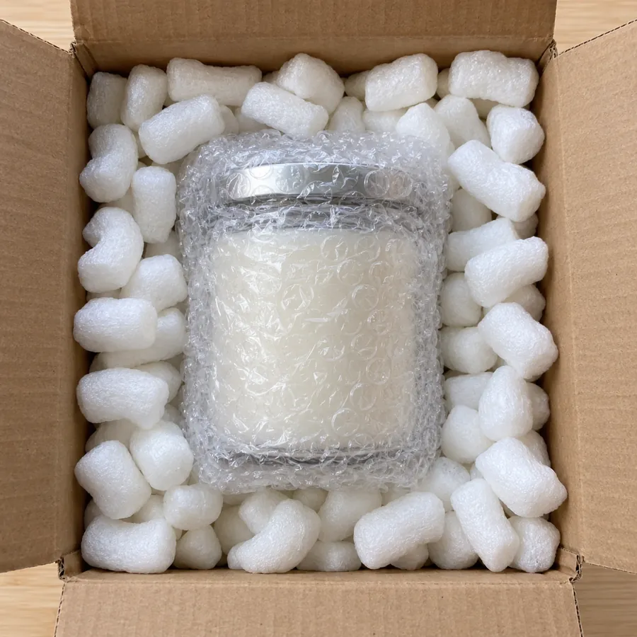 Bubble-wrapped jar candle centered in a box surrounded by packing peanuts