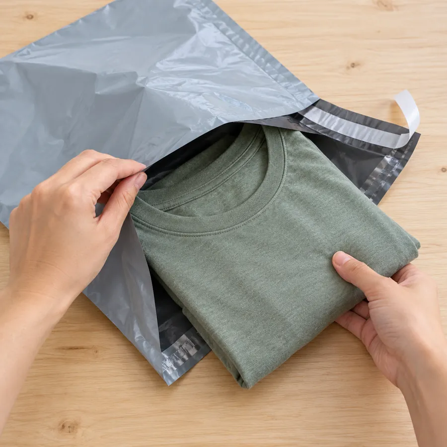Folded t-shirt being placed into a gray poly mailer