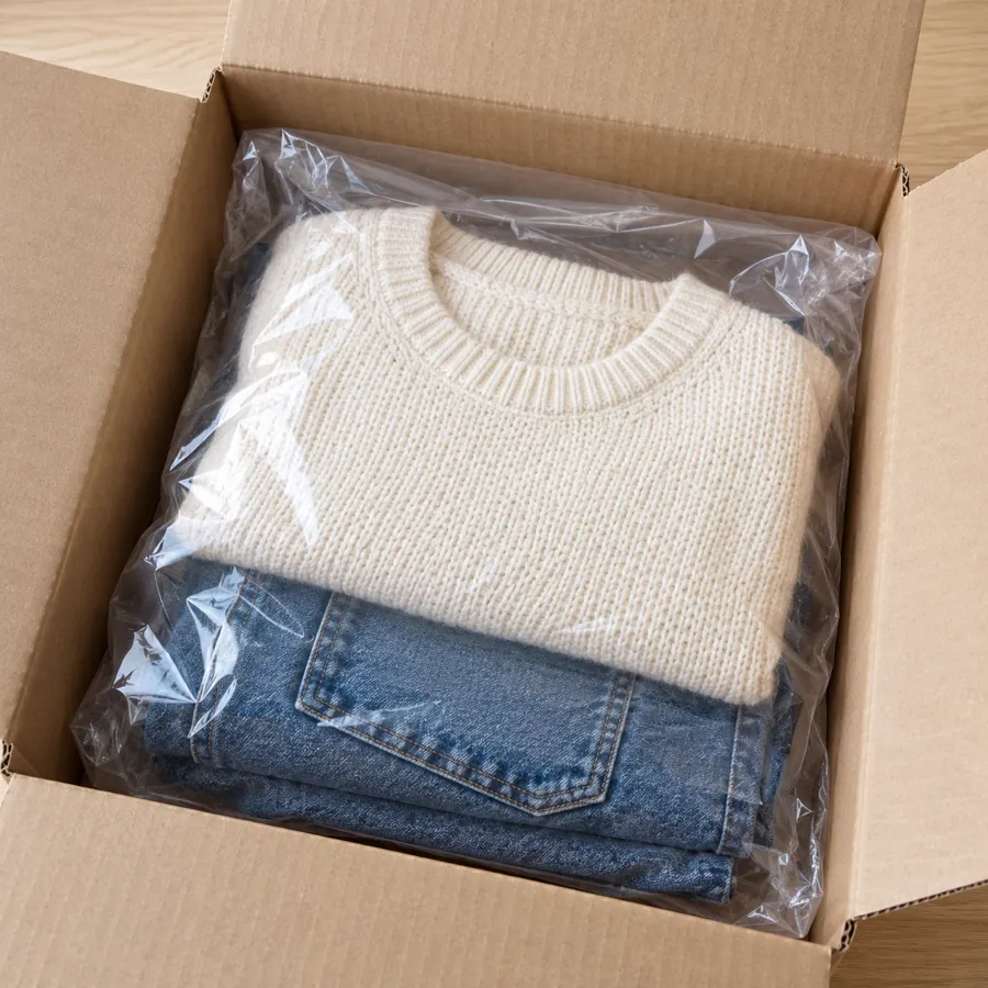 Folded sweater and jeans in a clear plastic bag inside a cardboard box