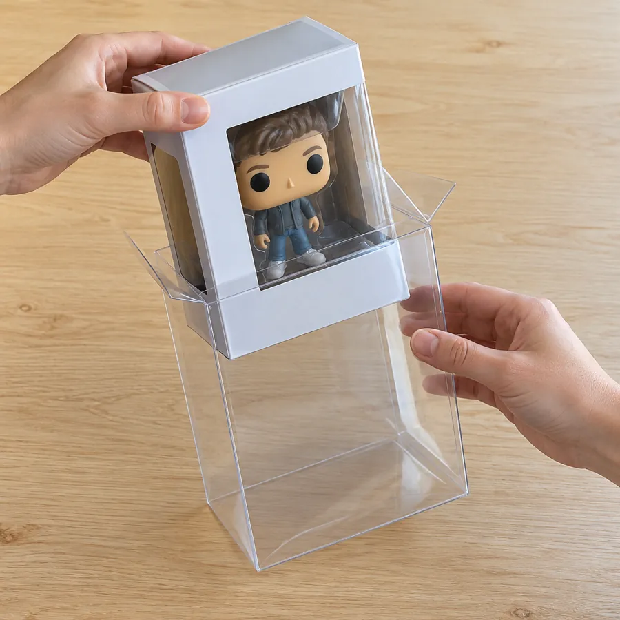 Hands sliding a boxed vinyl figure into a clear plastic box protector