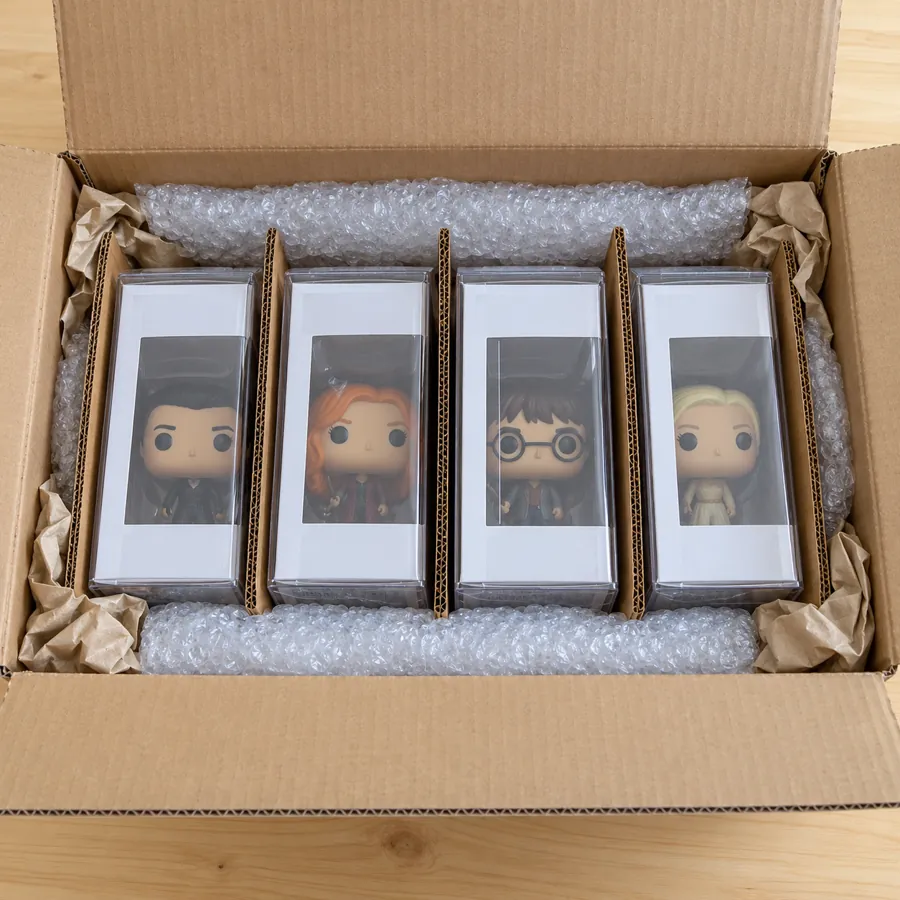 Four boxed figures in protectors standing upright in a shipping box with cardboard dividers